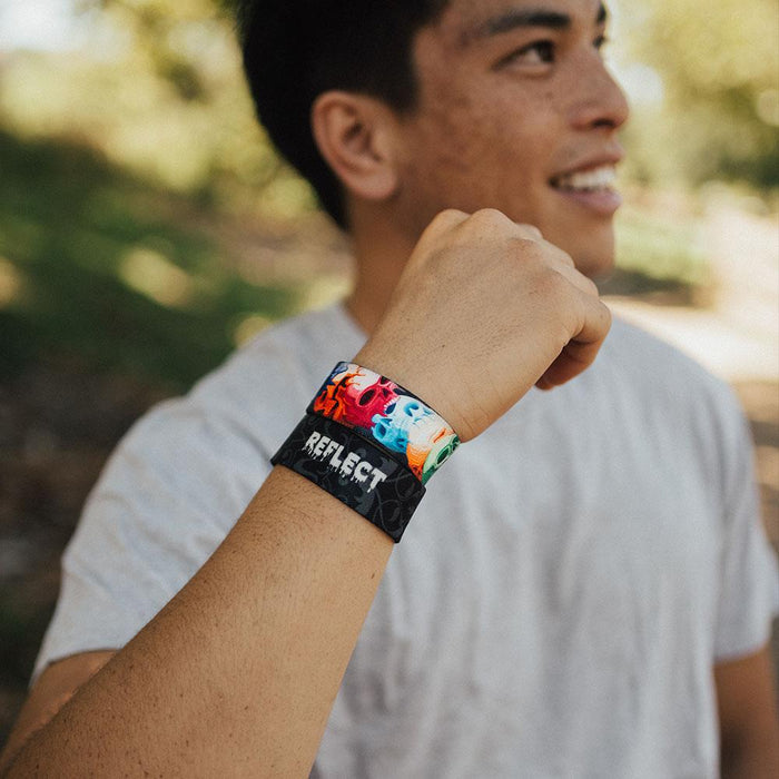 Young adult male wearing two reflect ZOX with hand close to head. The male is smiling. One ZOX shows the inside while the other shows the outside