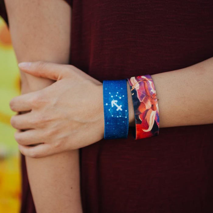 Lifestyle close up image of someone holding their arm and wearing 2 Sagittarius straps on their wrist