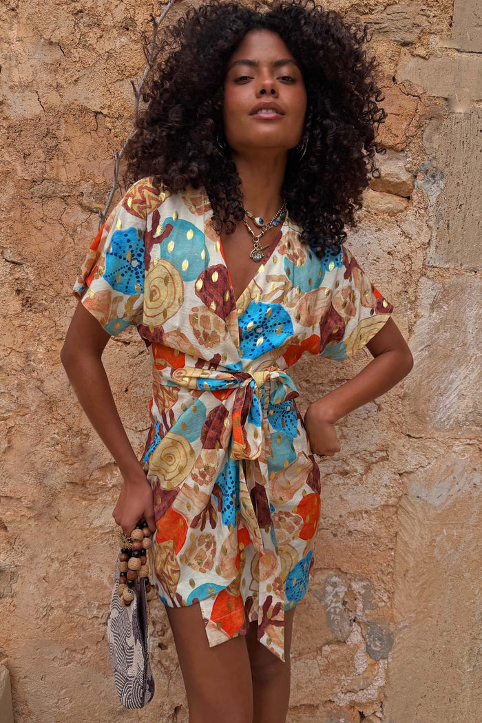 Shell Mini Wrap Dress featuring an abstract blue and orange shell print, metallic details and flutter sleeves on a model.