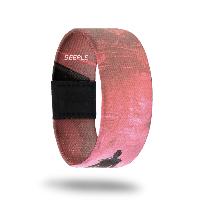 outside product photo of a wristband named Show Up designed by Beeple. It is mainly pink and red and features a darker silhouette of a warrior walking down a road to a larger lighter colored warrior that appears to be in the sky