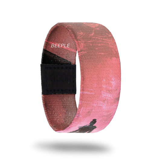 outside product photo of a wristband named Show Up designed by Beeple. It is mainly pink and red and features a darker silhouette of a warrior walking down a road to a larger lighter colored warrior that appears to be in the sky