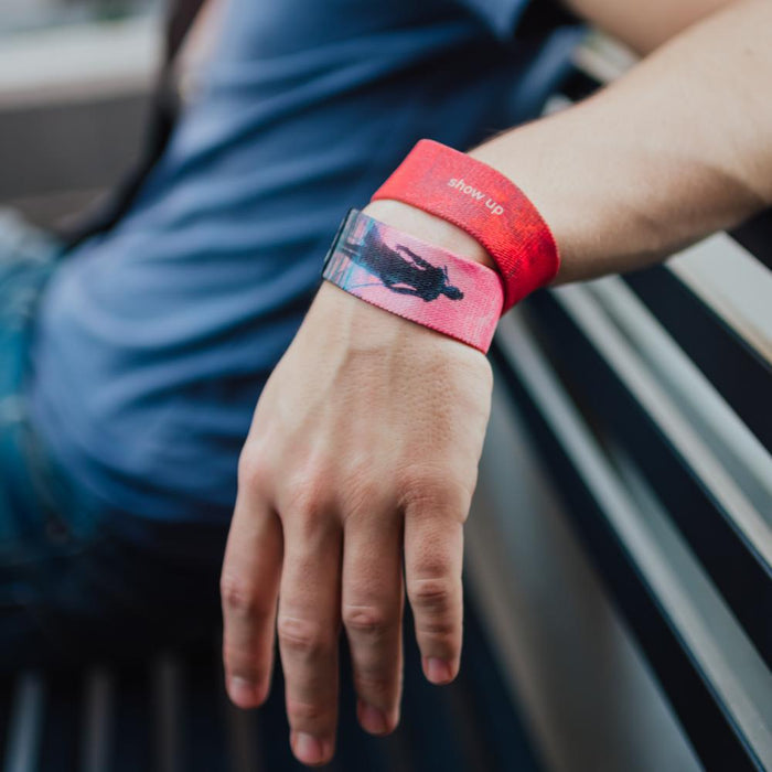 A lifestyle photo of a man wearing two Show Up wristbands at the same time. One showing the inside and the other showing the outside while his hand is relaxed on a bench