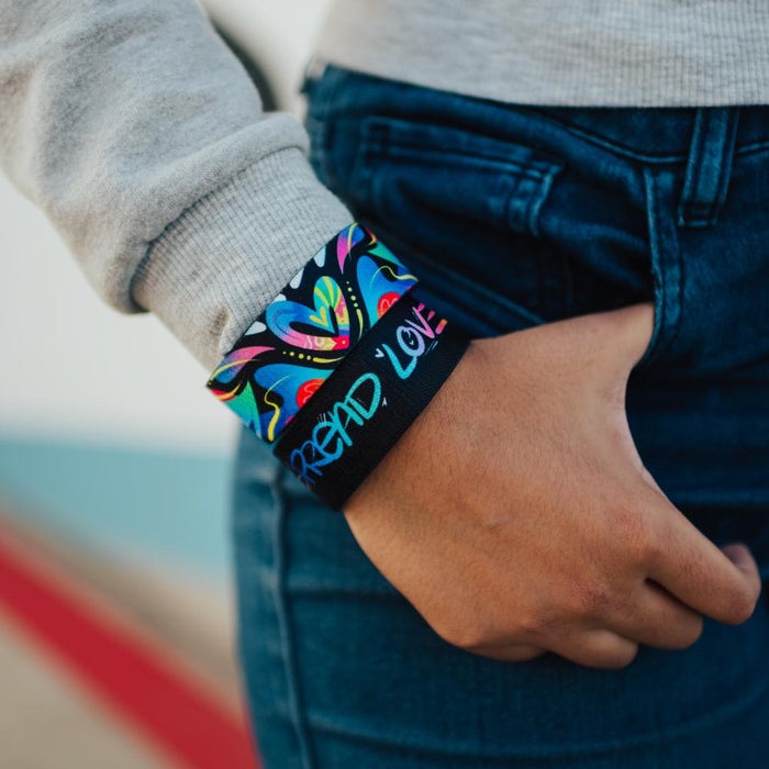Lifestyle close up image of model's hand in their pocket and wearing two Spread Love straps
