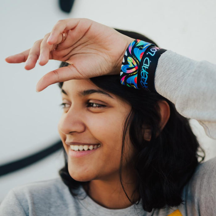 Lifestyle image of model resting arm on their head wearing two Spread Love straps