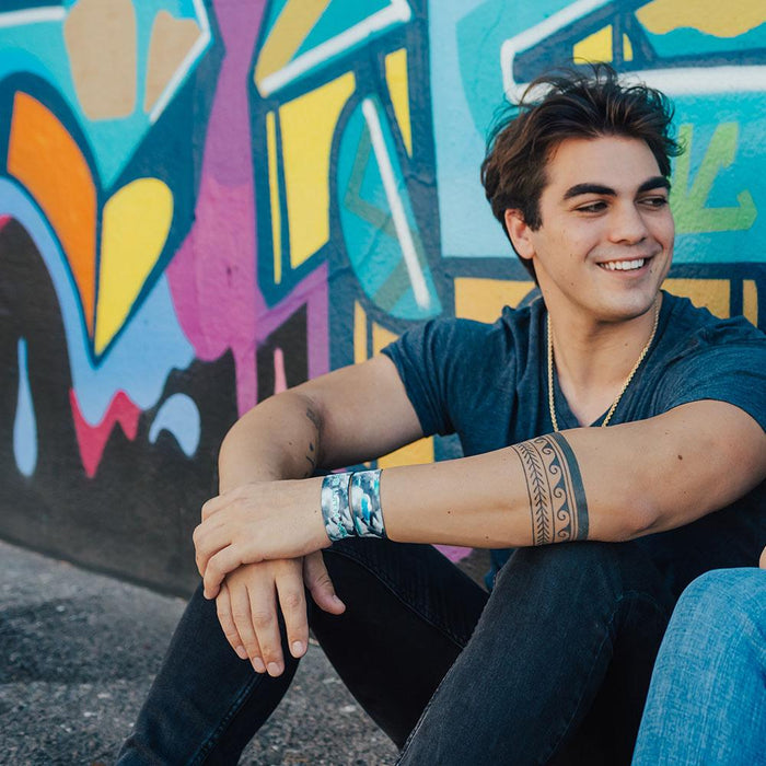 Lifestyle image of sitting model with arms crossed in front of their knees and 2 Take Me With You on their wrist