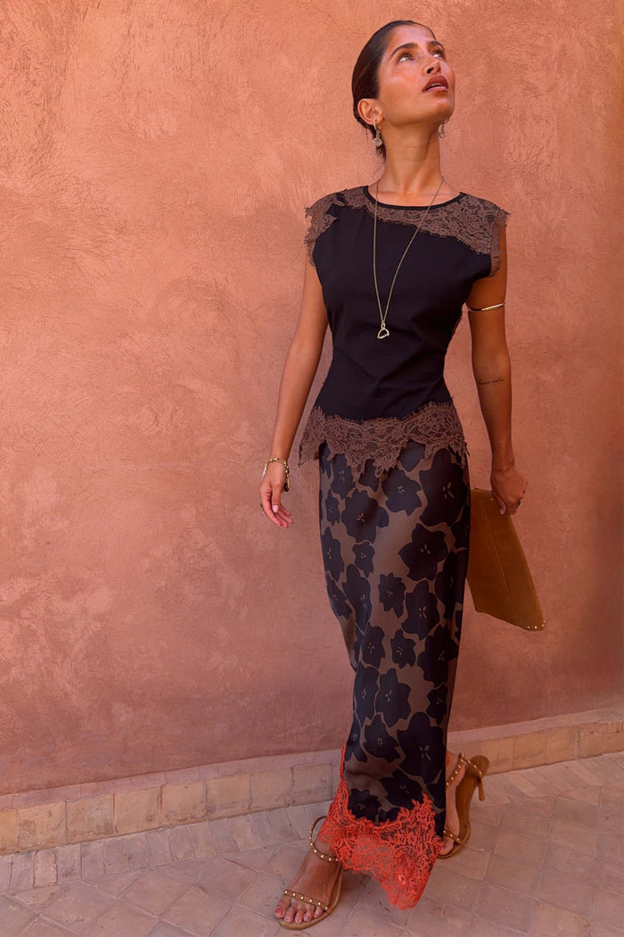 Tan Jaden Floral Maeva midi skirt featuring a bias-cut fit and orange lace hem, worn by a model against a clay wall.
