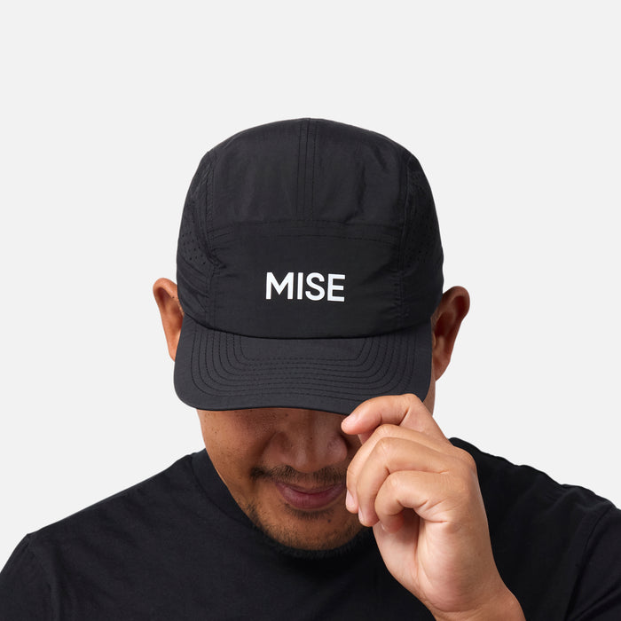 The Run Hat gallery position 1 showing black cap front with white MISE logo worn by model adjusting brim