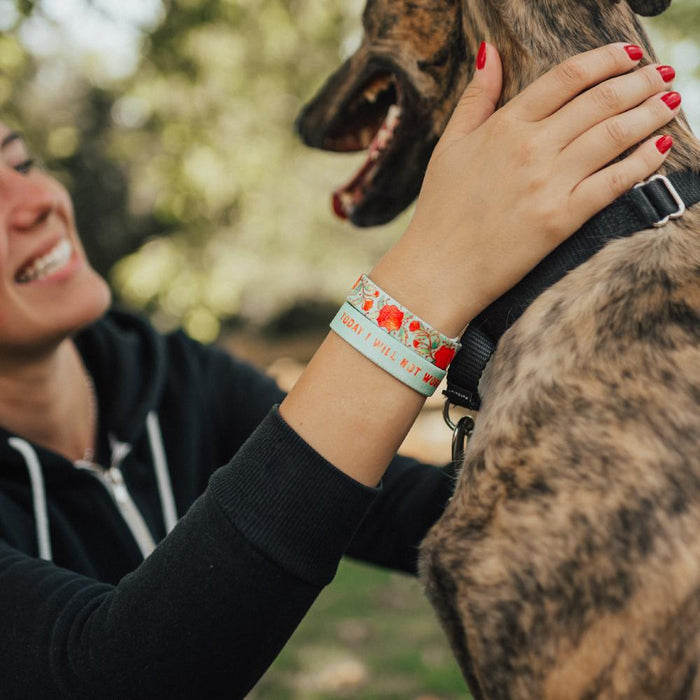 lifestyle image showing a woman wearing two Today I Will Not Worry's. One shows the front design while the other shows the name on the inside while petting a dog