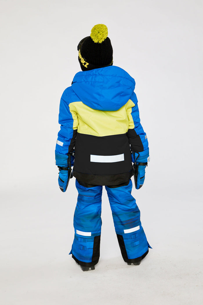 Child in the royal blue and yellow TEKNIK snowsuit, back view