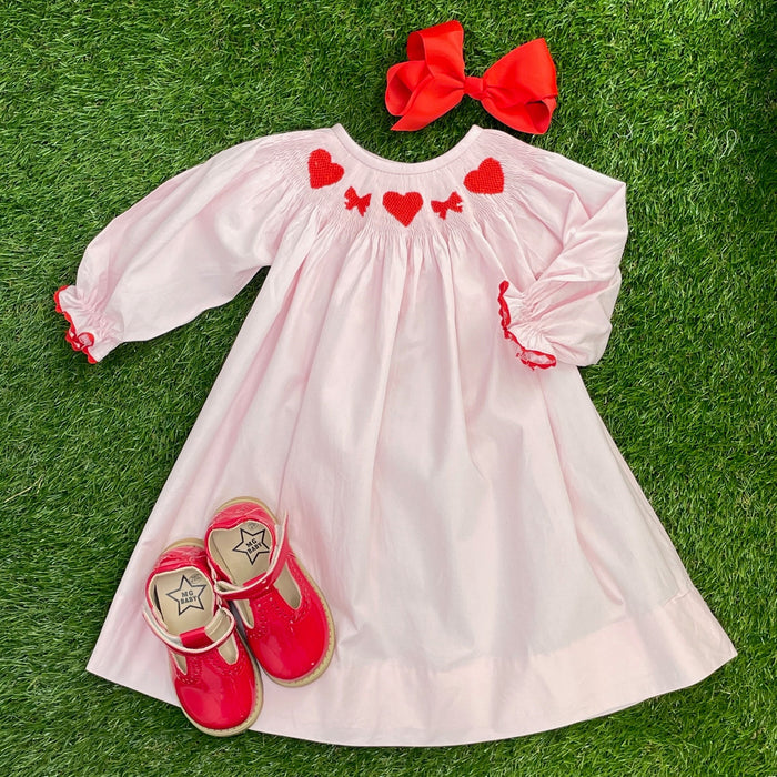 A long-sleeve pink smocked dress with red hearts and bows