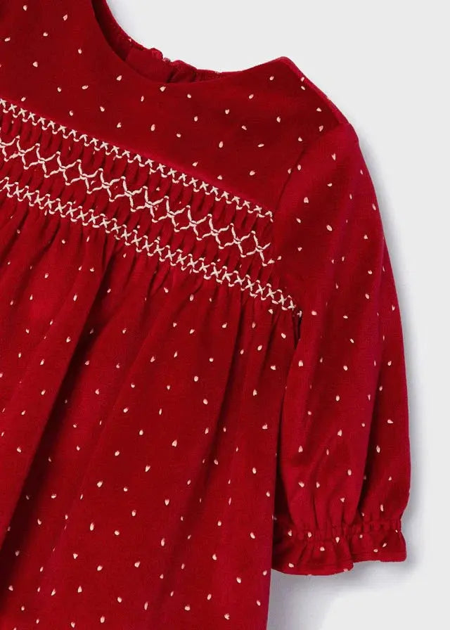 Close view of red Mayoral velvet dress with cream dots, smocking and ruffled cuff