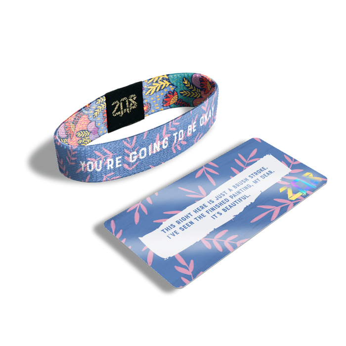 Product photo of the inside of You're Going To Be Okay. It is purple with pink leaves on branches with white text overlaying you’re going to be okay and its card saying ‘This right here is just a brush stroke. I’ve seen the finished painting, my dear. It’s beautiful.’